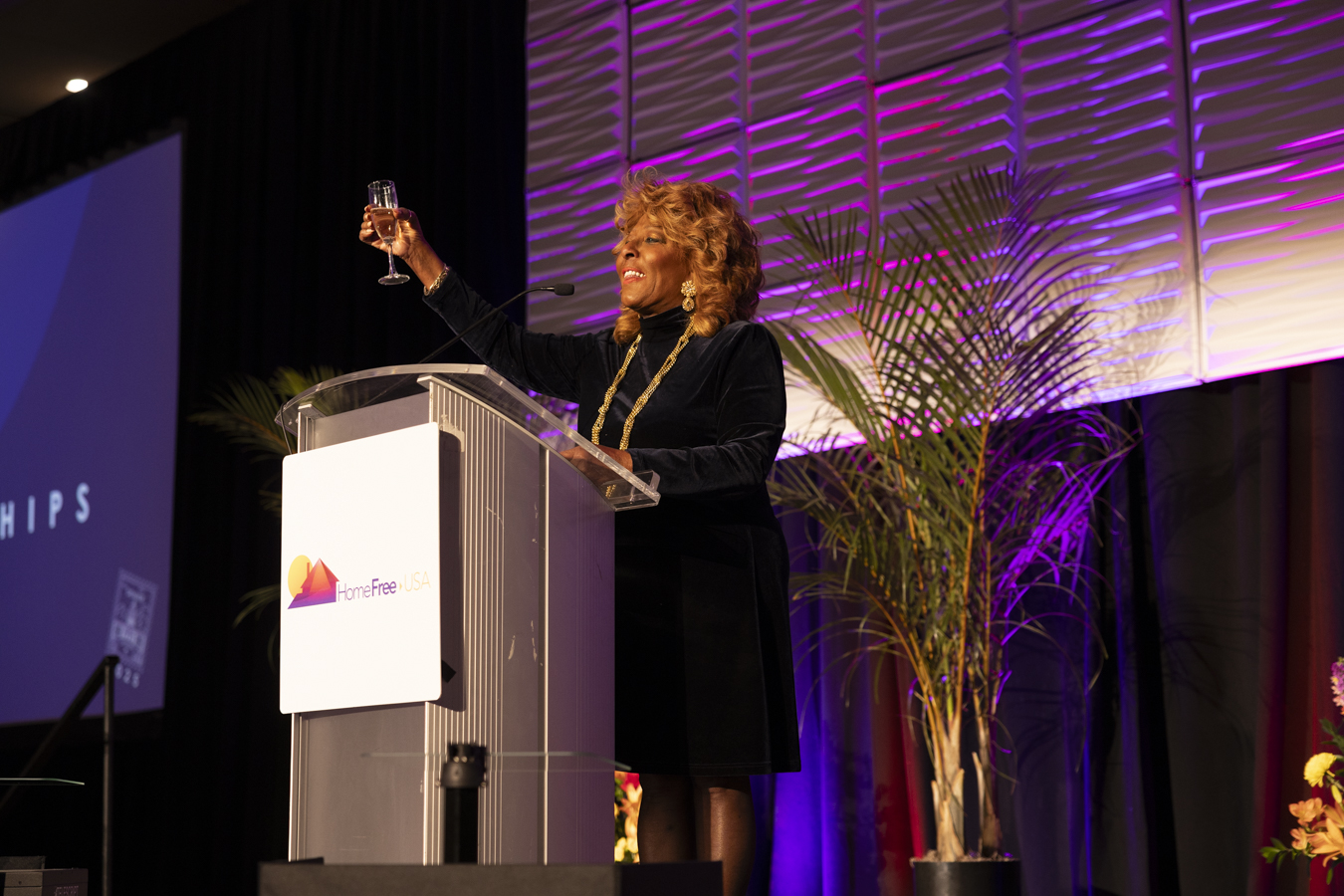 Marcia Griffin raising a toast on stage at a HomeFree-USA event